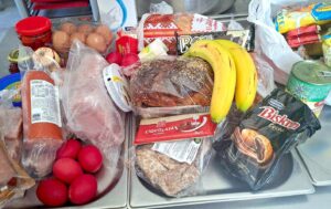 Pachet cu alimente de Paște, cu ouă roșii, banane, cozonac, mezeluri și alte produse, pregătit pentru beneficiarii cantinei sociale din Constanța